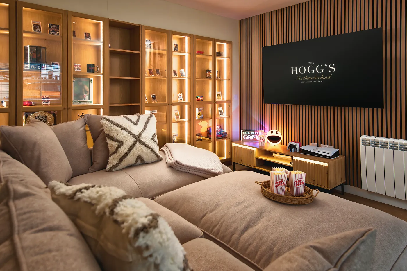 Cinema room with a big corner sofa, a wall-mounted screen and lit display shelves
