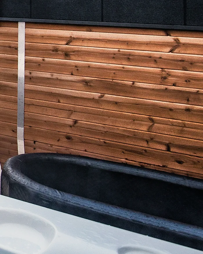 The black cold plunge tub beside the timber sauna, just behind the hot tub