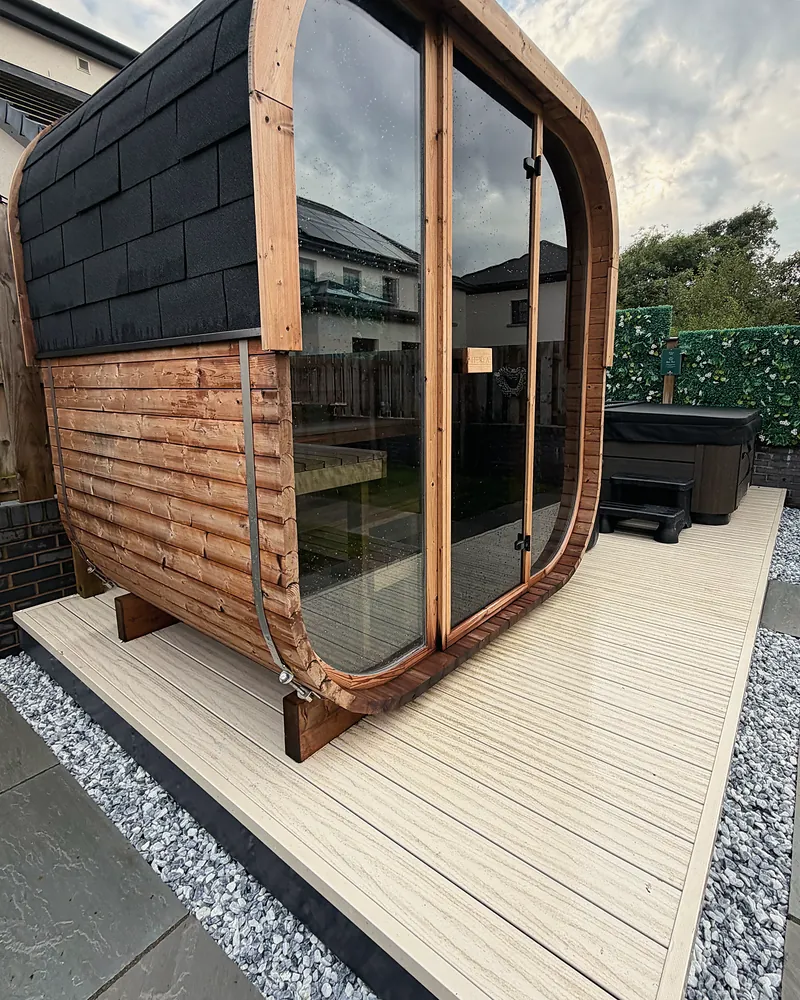 The glass-fronted timber garden sauna on its decking, with the hot tub and the green living wall behind