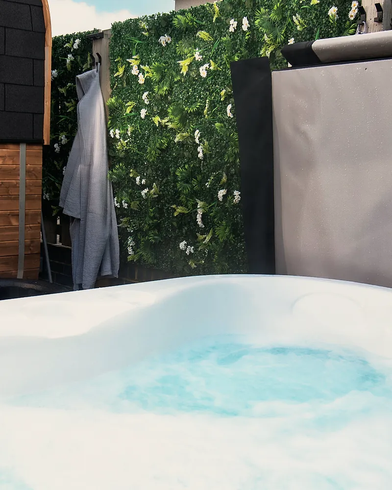 The private hot tub bubbling, with a robe hanging on the green living wall behind